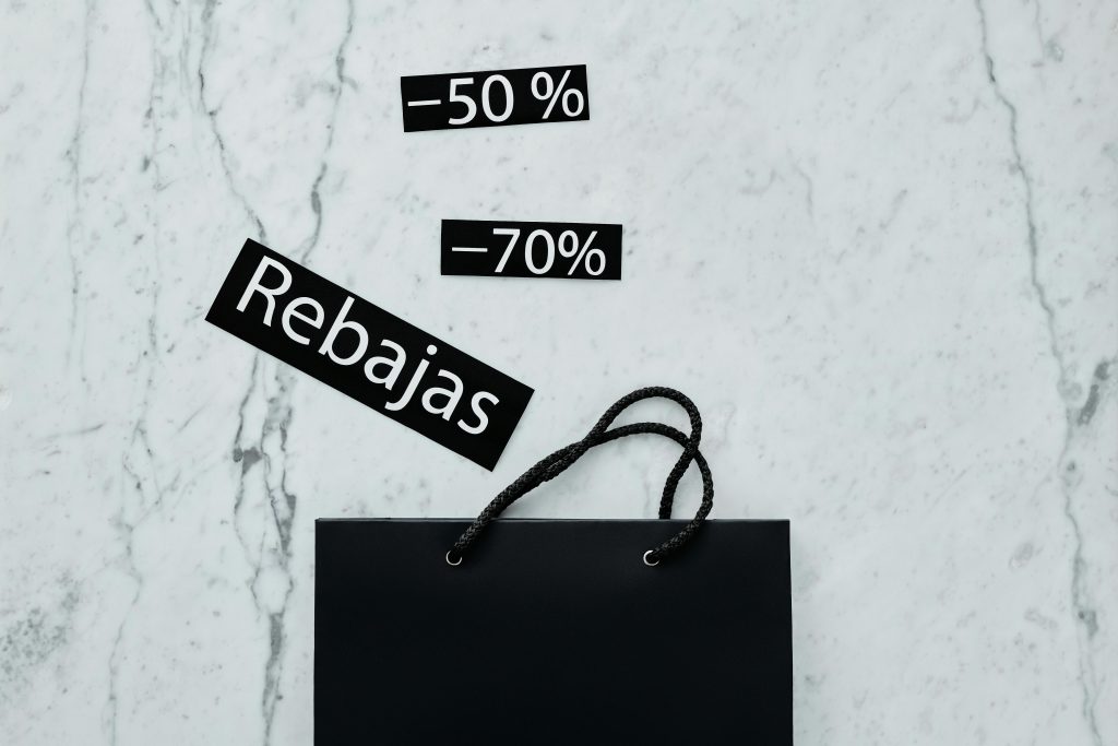 Modern flat lay featuring a black shopping bag with 50% and 70% sale tags on a marble surface.
