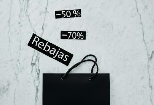 Modern flat lay featuring a black shopping bag with 50% and 70% sale tags on a marble surface.