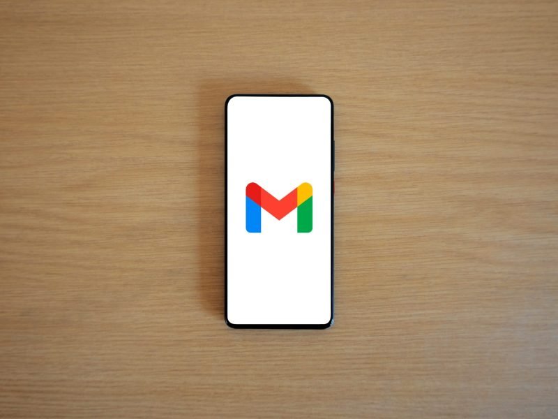 A smartphone displaying the Gmail app logo on a wooden surface, viewed from above.