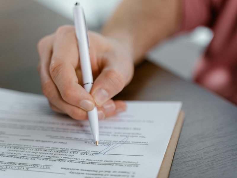 Detailed view of a hand writing a signature on an official document with a ballpoint pen.