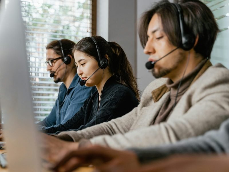 Three call center agents working diligently with headsets in an office setting, showcasing teamwork.